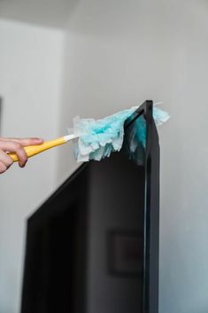 a person is cleaning the television with a yellow and blue duster on top of it