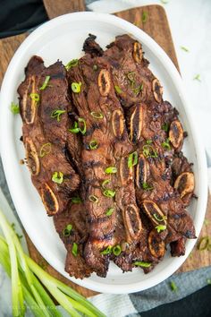 a white plate topped with sliced up meat and green onions next to a wooden cutting board