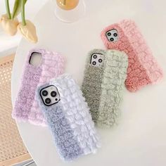 three cell phone cases sitting next to each other on a white table with flowers in the background