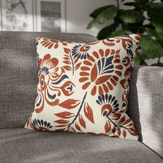 an orange and blue pillow sitting on top of a gray couch next to a potted plant