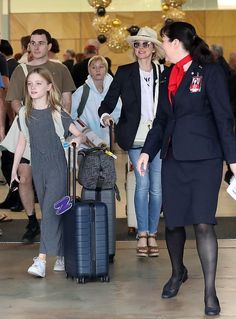 two women and one girl are pulling luggage through an airport terminal while other people look on