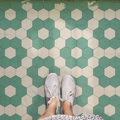 a person's feet in white and green tennis shoes on a tiled floor with hexagonal tiles