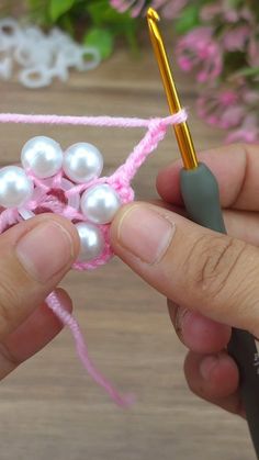 someone is crocheting some pearls on a piece of pink yarn with a pen