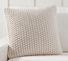 a white couch with a knitted pillow sitting on it's backrest,