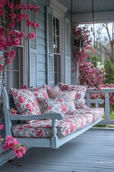 a porch swing with pink flowers hanging from it's sides and pillows on the back