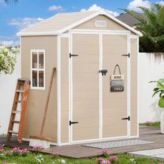 a garden shed with the door open and flowers in the foreground, next to it is a potted plant