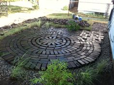 a circular brick garden design in the middle of some grass and rocks with plants growing on it