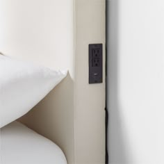 an electrical outlet on the wall next to a bed with white linens and pillows