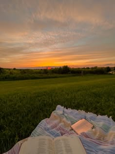 an open book sitting on top of a blanket in the middle of a grass field