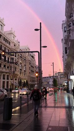 a rainbow in the sky over a city street with cars and people walking on it