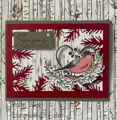 a red card with a bird on it and some pine branches in the background that says season's greetings