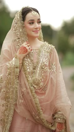 a woman in a pink outfit is standing on a dirt road wearing a veil and head piece