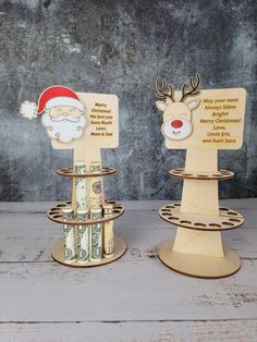 two christmas money holders with santa claus and reindeer heads on them, sitting on a wooden table