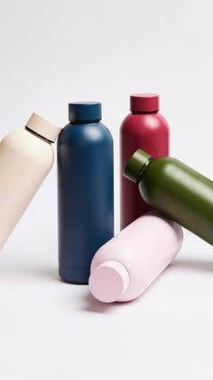 four different colored bottles are lined up on a white surface, one is empty and the other has a closed lid