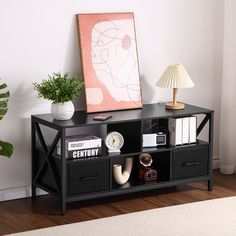 a black shelf with some books and other items on it next to a painting, lamp and plant