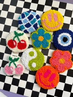 six crocheted buttons on a checkerboard surface with flowers and fruits in the center