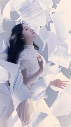 a woman in a white dress surrounded by sheets of sheet music and paper flying around her