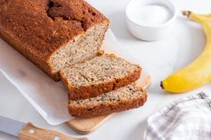 a loaf of banana bread sitting on top of a cutting board next to two bananas