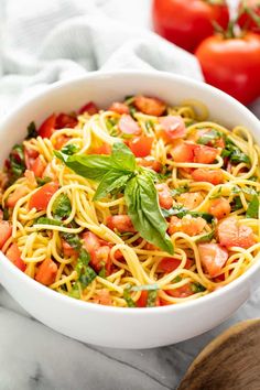 a white bowl filled with pasta and vegetables on top of a marble counter next to tomatoes