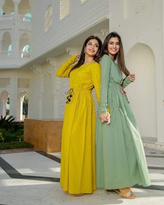 two young women standing next to each other in front of a white and yellow building