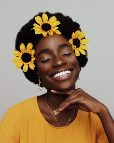 a woman with sunflowers in her hair smiles at the camera while wearing a yellow shirt