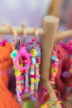 several colorful beads are hanging from a wooden rack with rings and tassels on it