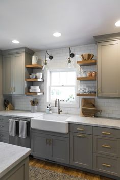 a kitchen with gray cabinets and white counter tops, open shelving above the sink