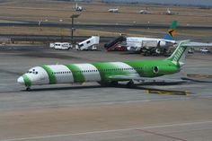 a green and white airplane is parked on the tarmac at an airport with other planes in the background