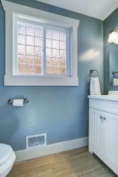 a white toilet sitting next to a window in a blue bathroom with tile flooring