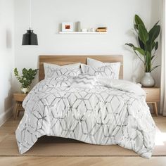 a bed with white comforter and pillows in a room next to a potted plant