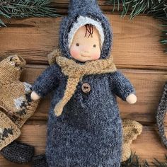 a knitted doll with a hat and scarf next to two mittens on a wooden surface