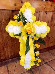 a cross with yellow and white flowers in front of a wooden wall on the ground