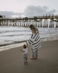 a woman holding the hand of a small child while standing on top of a beach