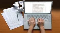 a person typing on a laptop computer next to an open book and paper with writing utensils