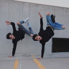 two young men doing tricks on their skateboards in an empty parking lot next to a concrete wall