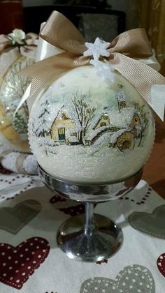 two christmas ornaments on top of a glass bowl with a bow around the neck and an ornament in the shape of a house