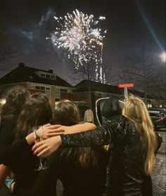 two women hug each other as fireworks go off in the background