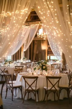 the tables are set up with white linens and lights hanging from the ceiling above them