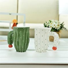 three cactus mugs sitting on top of a white table next to flowers and vases