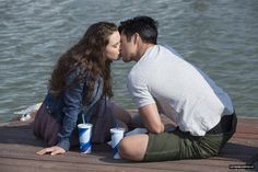 a man and woman sitting on a dock kissing