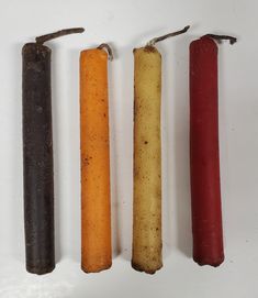 four different colored candles are lined up on a white surface, one is red, one is yellow and the other is brown