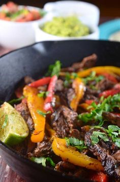 a skillet filled with meat, peppers and cilantros on top of a wooden table