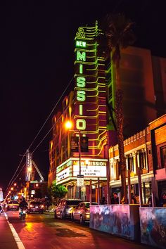 a city street at night with cars parked on the side and neon signs lit up