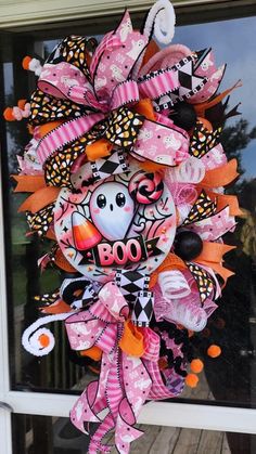 a pink and orange halloween wreath with boo on it's front door, hanging from the side of a window