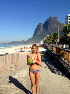 a woman standing on the beach holding a coconut and watermelon in her hand