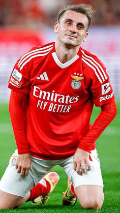 a man sitting on top of a soccer field wearing a red shirt and white shorts