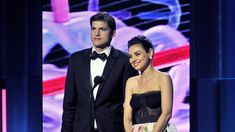 a man and woman standing next to each other in front of a stage with an award