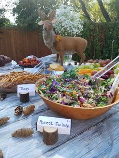 a wooden table topped with lots of different types of salads and fruit next to a deer figurine