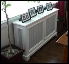 a white cabinet with pictures on it next to a potted tree