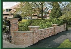 a brick wall and gate in front of a house with green plants growing on it